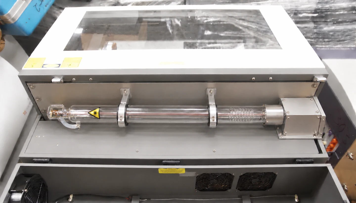 Reference illustration of a glass CO₂ tube supported by two metal ring mounts on the rear aluminium back plate, with an enclosed beam housing on the right